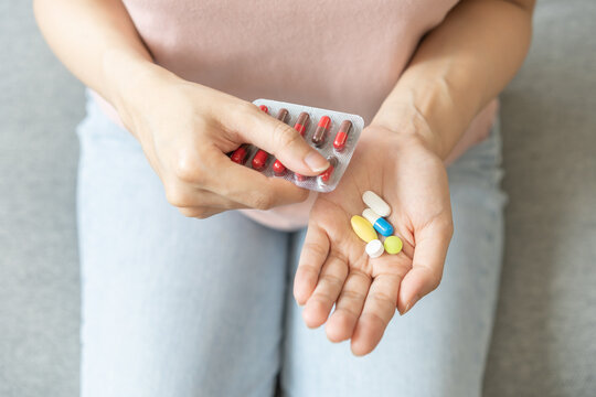 Sick ill asian young woman, girl hand taking tablet pill capsule out from blister pack, painkiller medicine from stomach pain, head ache, pain for treatment, take drug or vitamin at home, health care.