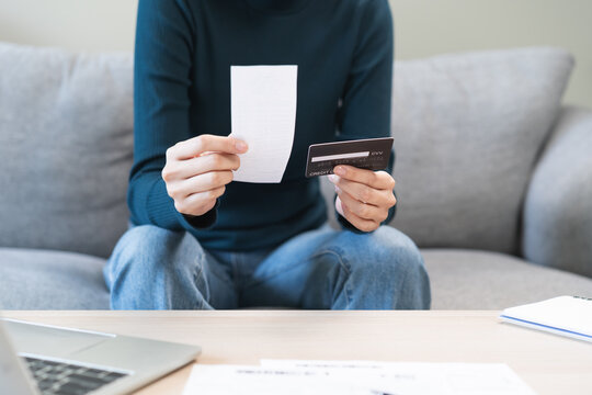 Stressed asian young business woman, employee calculate expenses of monthly, hand holding bills, receipt and credit card to payment on table at home. Financial, finance of banking concept.