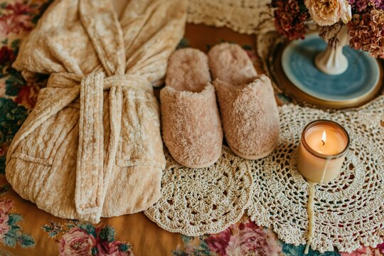 Plush velvet robe and fuzzy slippers beside a glowing candle on lace doilies for home wellness and lifestyle brands