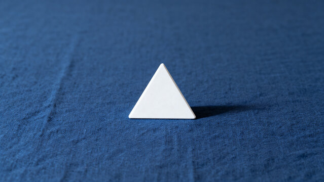 equilateral. Single white equilateral triangle object on deep blue linen, calm still life for editorial concept, lifestyle magazines.