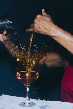 Amber liquid splashing into a coupe glass while being poured by a bartender with dark skin for hospitality and bar advertising