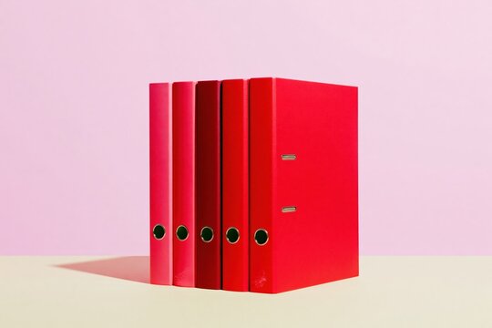 Row of vibrant red and pink ring binders standing on a smooth desk surface for document management and office organization concepts
