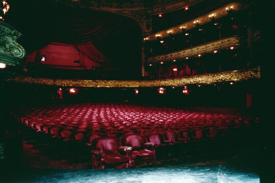 Ornate historic theatre interior with rows of plush red velvet seats facing a draped stage for performing arts and entertainment concepts