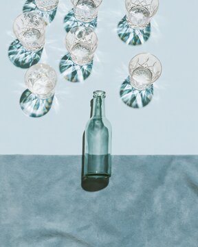 A slim glass bottle and faceted crystal drinking glasses on a soft blue surface with prismatic light reflections for minimalist beverage branding