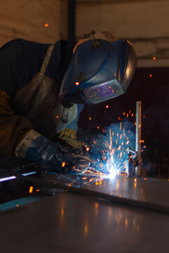 Professional welder wearing protective helmet welding metal with bright sparks