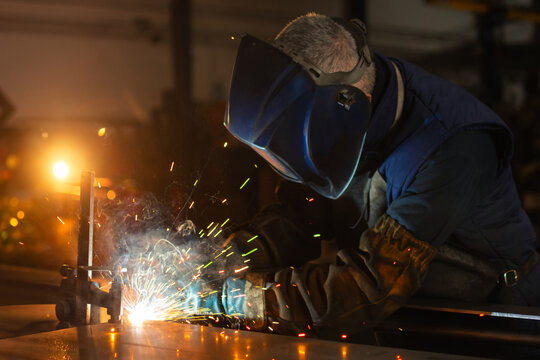 Close up of industrial welder in protective helmet welding metal with sparks