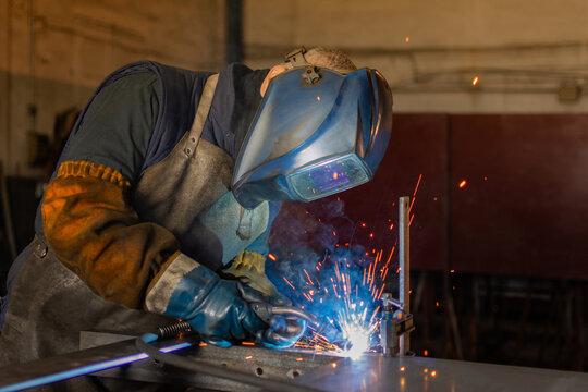 Industrial welder in safety helmet welding metal components with flying sparks