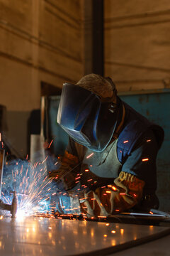 Close up industrial welder wearing safety helmet and welding metal with sparks