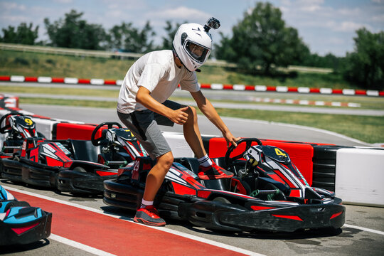 Teenage boy giving a thumbs up while stepping into a go-kart on a track