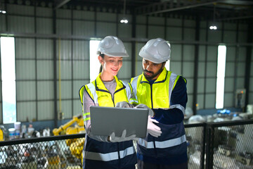 Fototapeta premium Workers discuss plans inside a factory while looking at a laptop during working hours