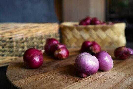 This photo shows several shallot cloves both peeled and unpeeled on a wooden cutting board, as well as a pile of shallots in a woven bamboo basket.