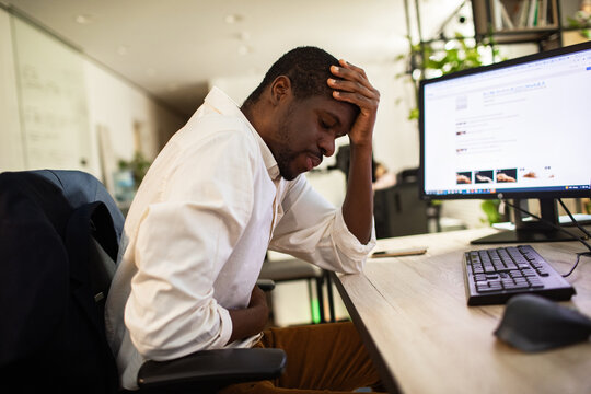 Tired office worker holding head at computer desk