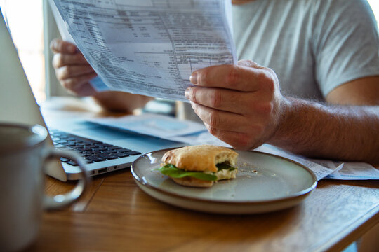 Person reviewing household bills at kitchen table with laptop