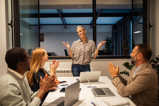 Colleagues applaud female leader during office meeting