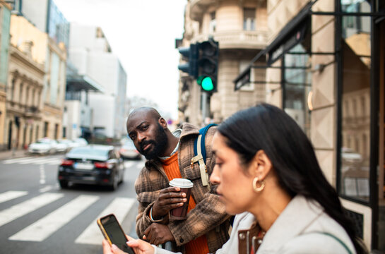 Man with coffee glancing at woman's phone on city street