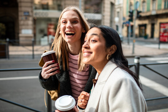 Two young women laughing with takeaway coffee on a city street