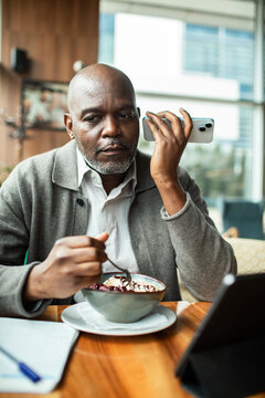 Mature man eating dessert and using smartphone at cafe table