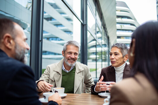 Mature colleagues discussing over coffee at outdoor cafe near modern office