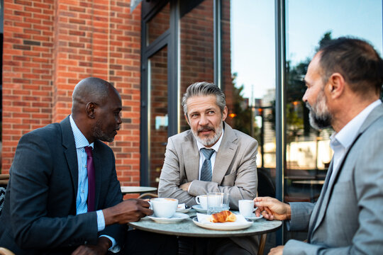 Three businessmen discussing over coffee at outdoor cafe