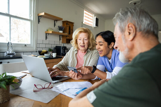 Caregiver assisting senior couple with online bill payment at home