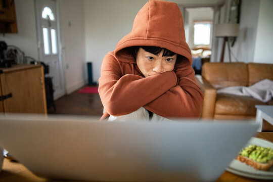 Woman in hoodie looking at laptop at home, feeling stressed