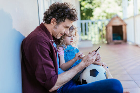 Father and daughter using smartphone on home porch