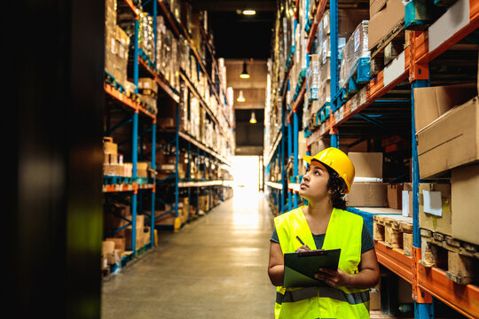 Warehouse worker inspecting inventory with clipboard in storage aisle