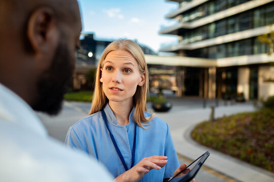 Female nurse consulting colleague outside hospital with digital tablet