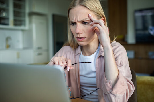Concerned young woman looking at laptop at home
