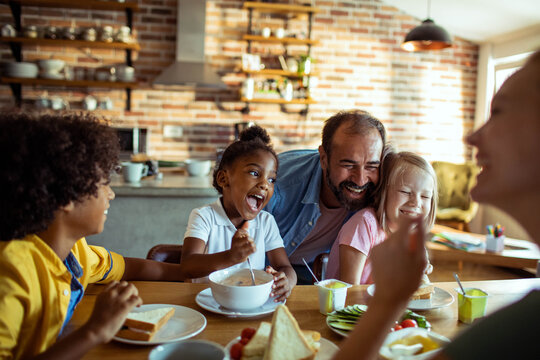 Smiling family with kids eating breakfast together at home kitchen