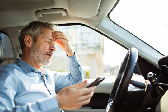 Frustrated mature man looking at phone inside car