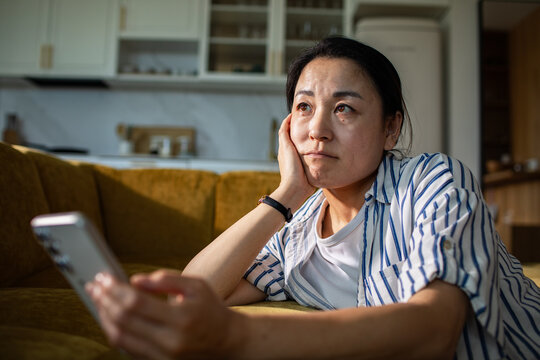Concerned woman checking phone on sofa at home