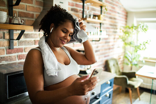 Woman using smartphone after home workout in kitchen