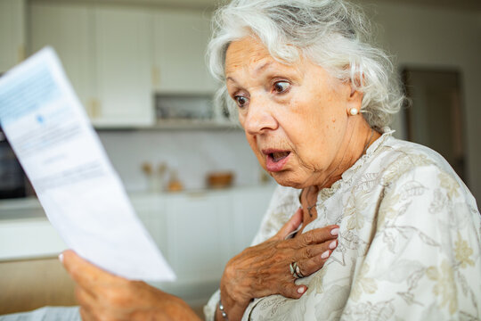 Shocked senior woman reading a bill in home kitchen