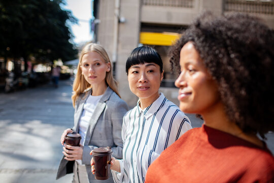 Three diverse businesswomen walking with coffee in city street