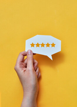 Hand holding five star rating speech bubble on yellow background