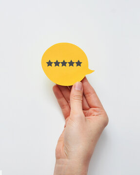 Hand holding five star rating speech bubble on yellow background