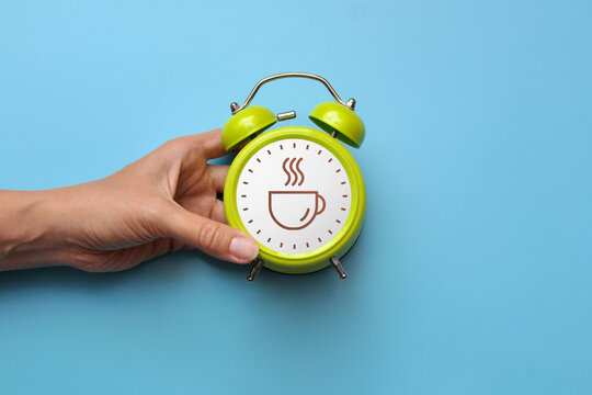 Hand holding alarm clock with coffee cup icon, coffee break and work pause concept