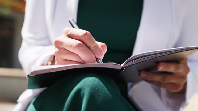 Close up of business woman hands writing with pen in notebook outdoors