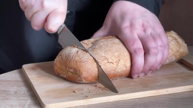 Slicing crusty bread with kitchen knife on wooden cutting board