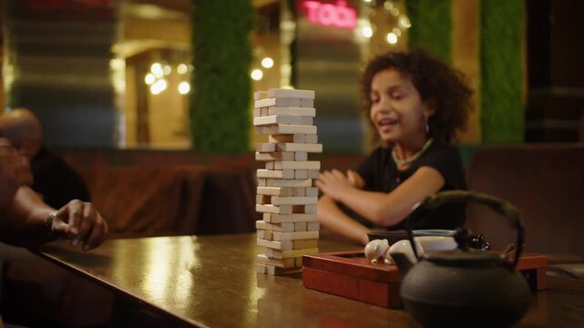 Black father playing wooden block tower game with daughter at cafe