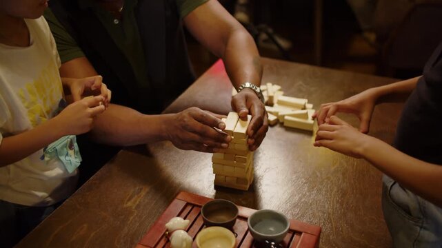 Black family playing wooden block stacking game at cafe