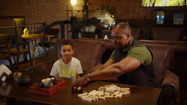 Black father and son playing dominoes together in cozy cafe