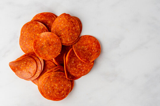 Closeup of uncooked pepperoni on a white marble surface 