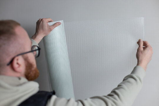 Man holding a roll of white plaster mesh for preparatory and painting works.