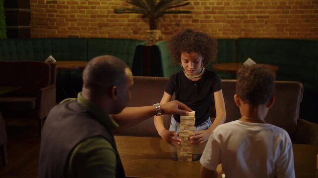 Black family playing wooden block tower game together at cafe