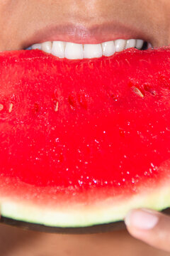 Vertical close up of woman biting into fresh ripe watermelon
