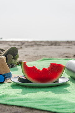Vertical bitten watermelon with hat sunglasses and water bottle on beach