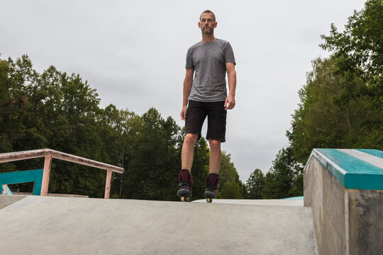 Active middle-aged man on inline skates standing on a concrete ramp at a skatepark on a cloudy day