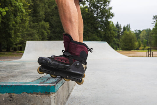 Close-up of aggressive inline skates on a mature man standing on a concrete ledge at a skatepark